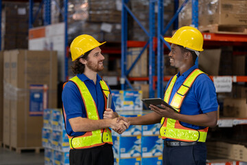 Two warehouse workers wearing safety gear shaking hands and smiling during successful logistics operation. Teamwork, partnership, and collaboration in warehouse and supply chain industry.