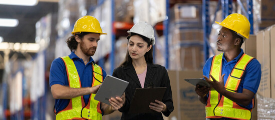 Warehouse workers and female supervisor using digital tablets and clipboard to discuss inventory management. Team collaboration concept in modern logistics and supply chain operations.