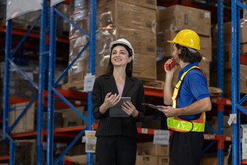 Female supervisor and warehouse man worker using tablets and walkie-talkie to discuss logistics operations. Team coordination in modern warehouse environment with smart inventory management.