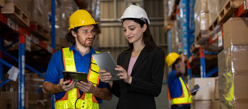 Warehouse supervisor and worker using digital tablets to review logistics data while another staff scans package. Concept of warehouse coordination, inventory tracking, smart supply chain operations.