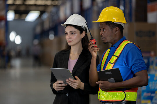 Warehouse worker man and female supervisor using walkie-talkie and tablet to coordinate operations. Concept of smart communication, teamwork and logistics efficiency in supply chain management. - Powered by Adobe