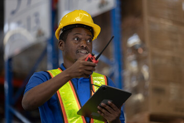 Smiling warehouse man worker in safety vest using mobile phone and digital tablet for communication and inventory coordination. Concept of smart logistics, operation, real time management.