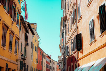 Fototapeta premium Narrow European Street with Tall Historic Colorful Buildings and Bright Sky Creating a Picturesque Urban Travel Scene Full of Charm and Architecture