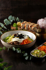 A beautifully arranged bowl filled with crisp vegetables, tender meat, and a fried egg lies next to an elegant plate of sushi. This inviting scene captures the essence of a delightful meal