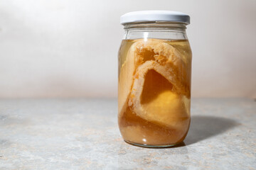 A glass jar containing a vinegar mother (SCOBY) for making vinegar, on a light-colored concrete-like surface.