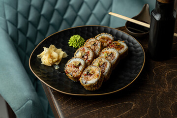 Fresh sushi rolls filled with savory ingredients rest on a beautiful black plate. A side of pickled ginger and wasabi add vibrant color to the scene in a warm, inviting space