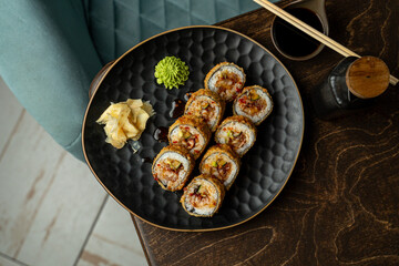 Savory sushi rolls sit elegantly on a textured black plate, accompanied by wasabi, pickled ginger, and a small dipping sauce, perfect for a delightful meal in a vibrant restaurant atmosphere