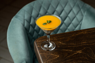 Bright orange drink sits elegantly in a martini glass, garnished with fresh mint. It captures...