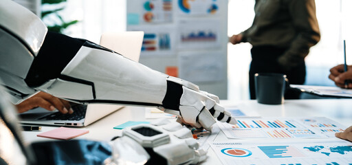 A robotic arm assists in a business meeting, focusing on data analysis and reports. The modern office showcases teamwork and technology in a collaborative environment.Noogenesis
