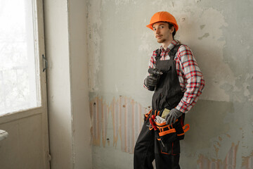 Portrait of Focused young worker in hard hat near wall with drill in building under renovation