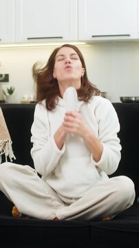 Young woman at home sings into comb like microphone dances and smiles with bold energy. Caucasian girl on sofa waves hand points at camera lip syncs chorus, enjoys music dream and star mood big joy