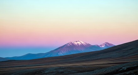 A scenic landscape featuring a mountain range with snow-capped peaks under a vibrant, colorful sunset sky. The foreground shows a grassy plain.