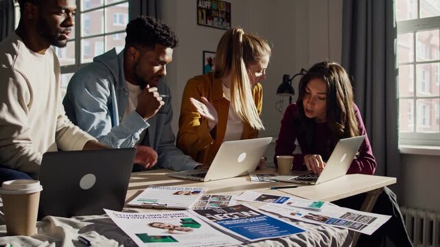 Diverse group of college friends collaborating on exam prep in their dorm room, engaging in a brainstorming session while using their laptops