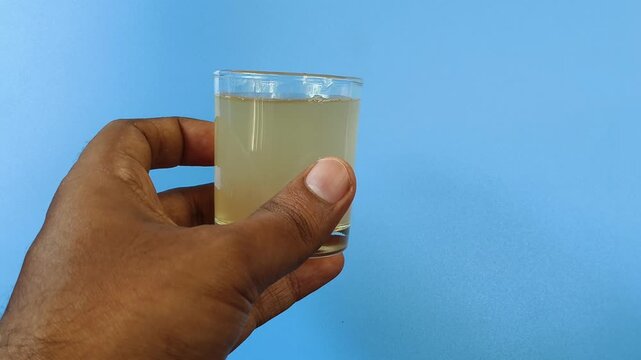 Hand holding glass with brown contaminated undrinkable dirty drinking water on a blue background with copy space. Conceptual photo about water crisis, scarcity, shortage, drought and less rainfall.