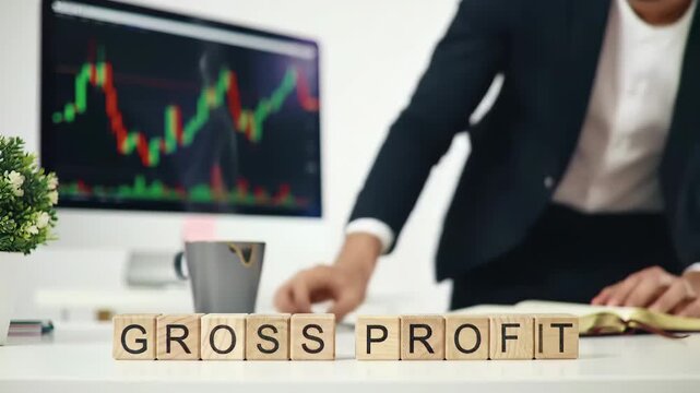 Gross profit inscribed on wooden blocks shows a man taking notes in office with candlestick charts. Focus on business investment financial growth and success.