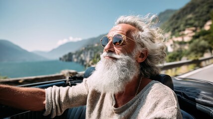 A smiling elderly man with long gray hair and sunglasses drives a classic convertible car on a scenic coastal road. The bright sun and beautiful water enhance the moment of relaxation and joy.