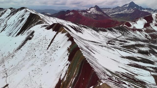 Aerial drone view of Rainbow Mountain Vinicunca in the Peruvian Andes, with multicolored peaks partly covered in snow. Located in the Cusco region, Peru.	
