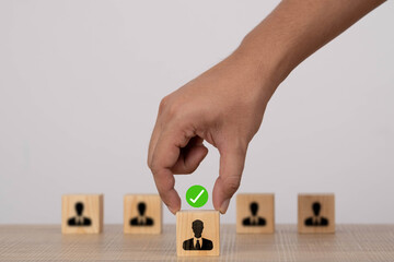Hand selecting a wooden block with a candidate icon and check mark, symbolizing recruitment, hiring decisions, human resources management, employee selection, and strategic business staffing.