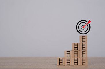 Wooden blocks arranged as steps with ladder icons leading to a target symbol represent goal achievement, progress, business growth, strategic planning, and motivation for reaching success step by step