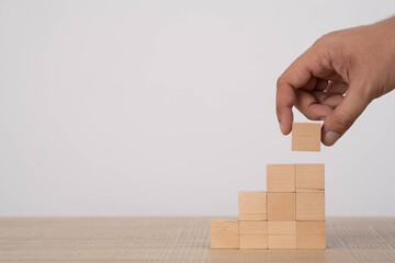 Hand placing a wooden block on a stepped structure symbolizes growth, progress, business development, strategic planning, and building success through step-by-step improvement and constructive effort.
