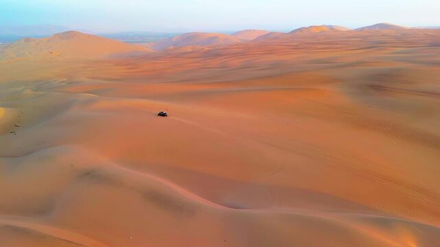Aerial drone view of a buggy moving across the desert landscape in the Huacachina oasis at sunset, Peru.