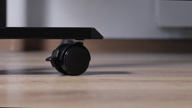 Black plastic caster wheel with an integrated locking mechanism, providing flexible mobility and firm stability for adjustable modern furniture on wooden flooring