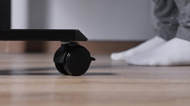 Black furniture caster wheel securely positioned on light wooden floor, offering smooth mobility for modern office and versatile home setups