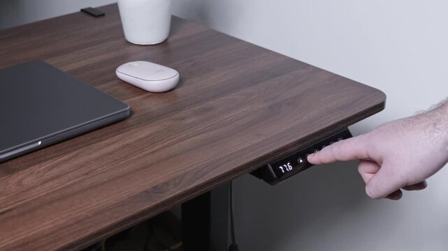 Male hand adjusting a modern wooden adjustable standing desk's height controller displaying 79.0, promoting ergonomic workspace and healthy productivity in a flexible home office setup