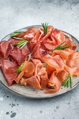 Italian charcuterie platter with bresaola, prosciutto, coppa and green olives arranged with rosemary on a textured gray background.