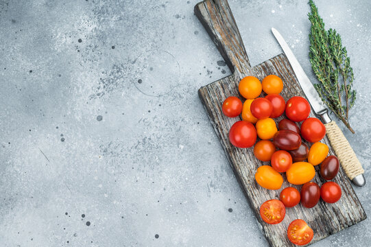 Colorful mix of cherry tomatoes on a rustic wooden board with herbs and knife on a textured gray background perfect for food templates.