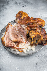 Crispy roasted pork knuckle with sliced tender shank meat served on sauerkraut over gray stone background with mustard and fork styling.