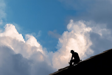 Roofer silhouette working on residential roof under dramatic blue sky