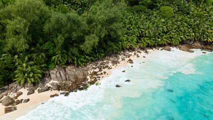 Tropical beach with clear turquoise ocean waters, large rocks, and lush greenery. Seychelles, Mahe. Anse Intendance.