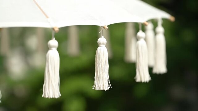 White parasol with decorative tassels against a blurred green backdrop