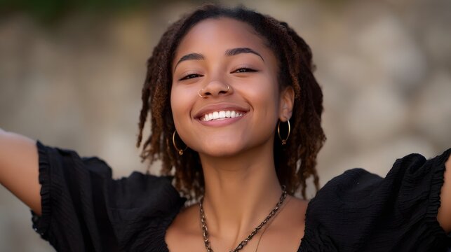 Young woman with dreadlocks smiling joyfully with arms outstretched outdoors