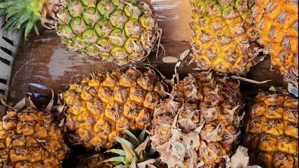 Fresh ripe pineapples display at tropical fruit market. Golden yellow textured skin with green crowns arranged for sale. Overhead view of exotic produce selection. - Powered by Adobe