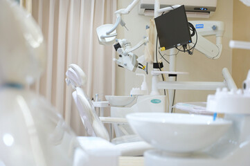 A dental operatory with white treatment chairs, a Zumax microscope, overhead light, and a wall-mounted monitor