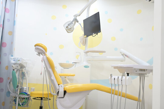 A pediatric dental operatory with a yellow chair, wall-mounted monitor, overhead light, and colorful polka-dot decor
