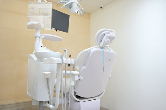 A white dental chair with its instrument unit, spittoon, overhead light, and monitor arranged in a minimalist treatment room