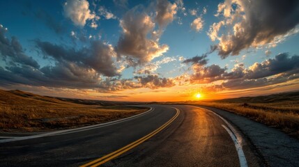 A road with a sunset in the background. The sky is cloudy and the sun is setting. The road is empty and the sun is low on the horizon
