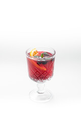Vibrant red sangria or punch cocktail in an ornate stemmed glass with orange, berries, and mint on a white background with ample copy space