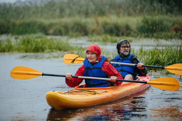 Senior couple kayaking paddling on water during rain