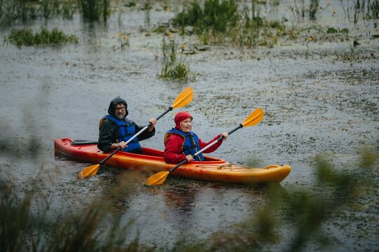Mature couple kayaking together enjoying rainy outdoor adventure - Powered by Adobe