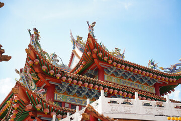 an ornate, traditional Chinese temple with red, gold, and green colors, adorned with pink lanterns, intricate carvings, and a white balustrade under a clear blue sky.