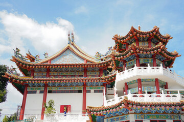 A ornate, multi-tiered Chinese temple with vibrant red and green roofs, detailed eaves, colorful patterns and dragons,  set against a bright blue sky with scattered clouds