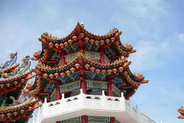 A ornate, multi-tiered Chinese temple with vibrant red and green roofs, detailed eaves, colorful patterns and dragons,  set against a bright blue sky with scattered clouds