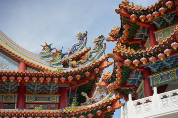 A ornate, multi-tiered Chinese temple with vibrant red and green roofs, detailed eaves, colorful patterns and dragons,  set against a bright blue sky with scattered clouds
