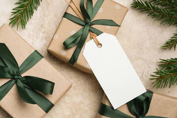 Christmas gift tag mockup with gift boxes featuring green ribbons and polka dot patterns, arranged on a textured surface with evergreen branches, perfect for holiday design projects