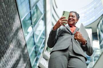 Portrait of a young  businesswoman woman using a smartphone mobile phone walking down the street,...