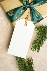 Christmas gift tag mockup with blank space, elegant gold gift box, green ribbon, and pine branches, perfect for holiday design projects and festive presentations